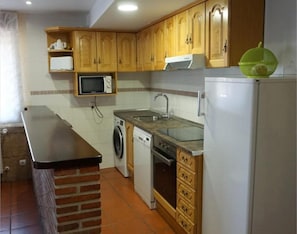 A kitchen with wooden cabinets, a microwave, a washing machine, a sink, and a refrigerator. - Country House 'La Casa Nueva' with Private Terrace, Wi-Fi and Air Conditioning (Abejar)