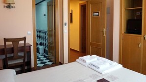 Habitación de hotel con cama, escritorio, silla, armario y baño visible a través de una puerta abierta.