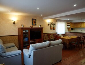 Olohuone, jossa on sohva, televisio sekä ruokailutila, jossa on tuoleja ja pöytä.
