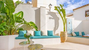 A white-walled outdoor seating area with a sofa, two round tables, and large potted plants. - Room 'Altea  01' with Shared Pool, Wi-Fi and Air Conditioning (Altea)