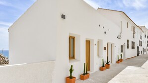 A white building with multiple doors and windows, a tiled roof, and potted cacti along the side. - Room 'Altea  01' with Shared Pool, Wi-Fi and Air Conditioning (Altea)