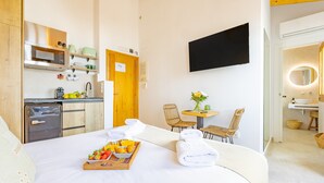 A hotel room with a bed, breakfast tray, towels, kitchenette, and a TV.