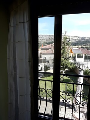 Un balcon doté d’une balustrade en métal, avec vue sur un quartier résidentiel composé de maisons et une colline en arrière-plan.
