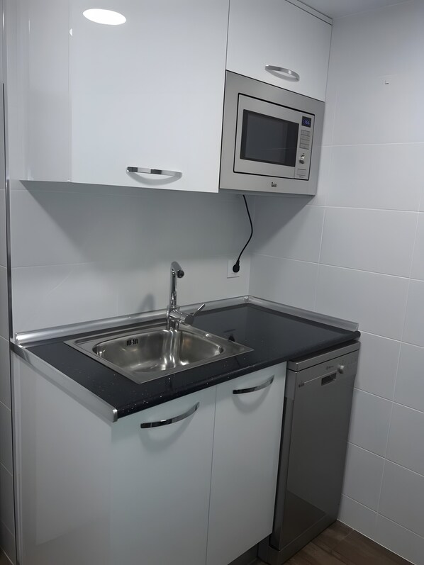A kitchen with a stainless steel sink, a microwave, and white cabinets.