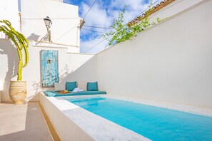 A pool area with a white wall, a blue door, and a seating area with cushions. - Room 'Altea  03' with Shared Pool, Wi-Fi and Air Conditioning (Altea)