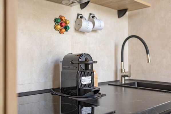 A coffee machine, a sink, and wall-mounted cups and a colorful object on a tiled wall.