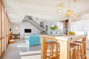 Un vaste espace de vie comprenant une table à manger en bois, des tabourets de bar, un escalier et un coin cuisine.