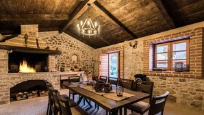 A rustic stone interior with a fireplace, wooden dining table, and chairs.