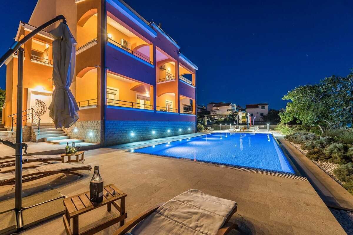 Un edificio de varios pisos con piscina, mobiliario exterior y una escalera que conduce a la entrada.