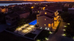 A residential area with houses, a swimming pool, and a view of the water and mountains at sunset.