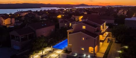 Zona residencial con casas, piscina y vistas al agua y las montañas al atardecer.