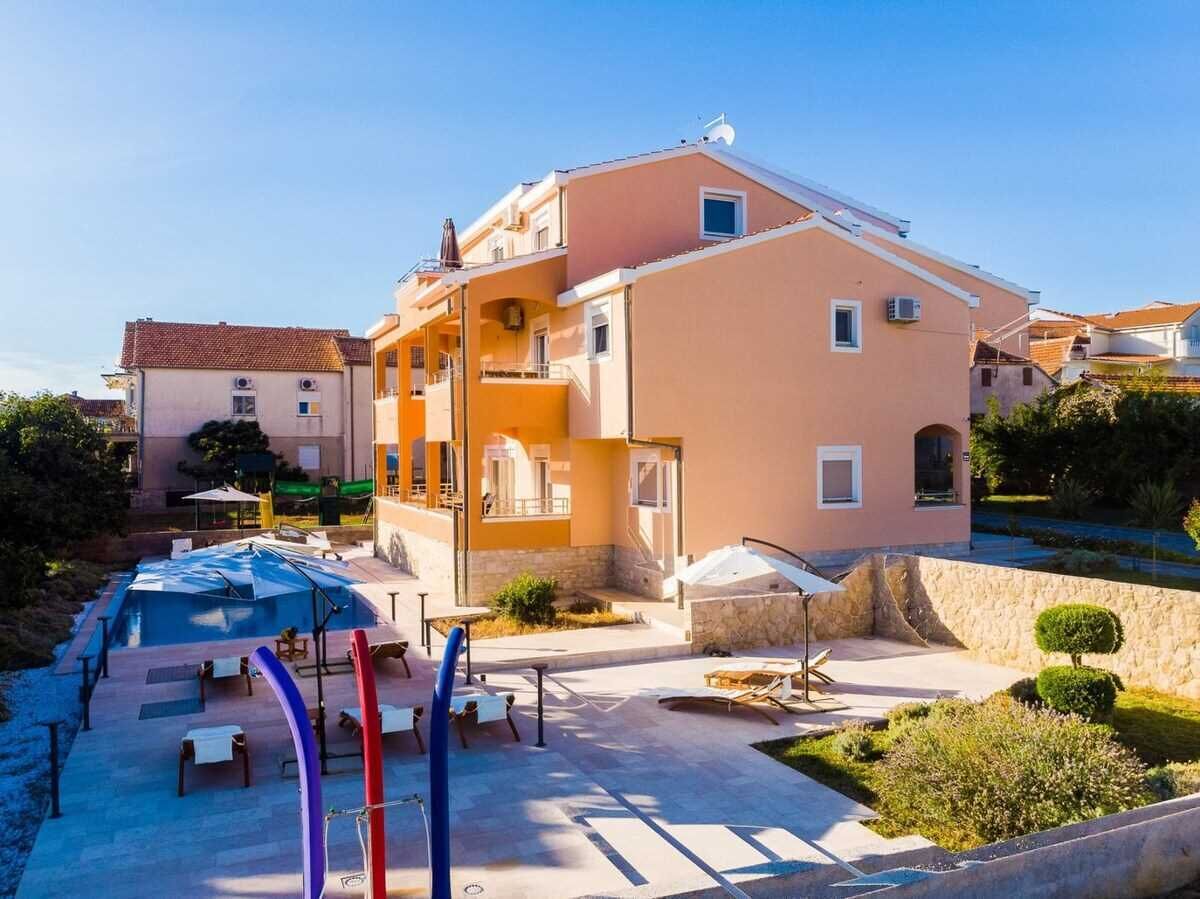 Un edificio de dos plantas con piscina, mobiliario de exterior y un jardín ajardinado.