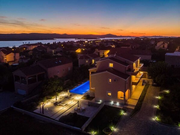 A residential area with houses, a swimming pool, and a view of the water and mountains at sunset.