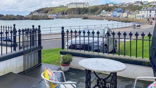 A balcony with a table and two chairs, overlooking a coastal area with a parked car and a building in the background. - 3 bedroom accommodation in Portpatrick, near Stranraer (Portpatrick, near Stranraer)
