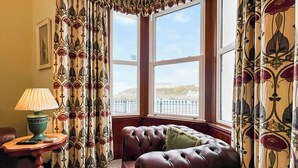A room with a large window, a leather sofa, a table with a lamp, and patterned curtains. - 3 bedroom accommodation in Portpatrick, near Stranraer (Portpatrick, near Stranraer)