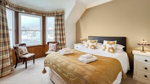 A hotel room with a large bed, a chair, a nightstand, and a window with curtains. - 3 bedroom accommodation in Portpatrick, near Stranraer (Portpatrick, near Stranraer)