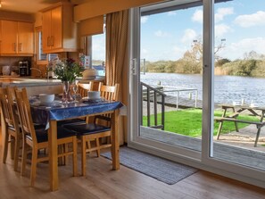 A dining area with a table set for four, a view of a lake, and a wooden deck outside. - 2 bedroom accommodation in Brundall (Brundall)