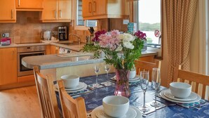 A modern kitchen with wooden cabinets, a coffee maker, and a dining area with a table set for four. - 2 bedroom accommodation in Brundall (Brundall)
