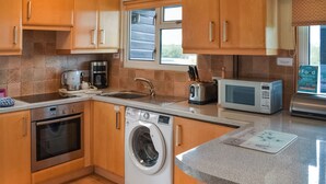 A compact kitchen with wooden cabinets, a stainless steel oven, a washing machine, a microwave, and a sink. - 2 bedroom accommodation in Brundall (Brundall)