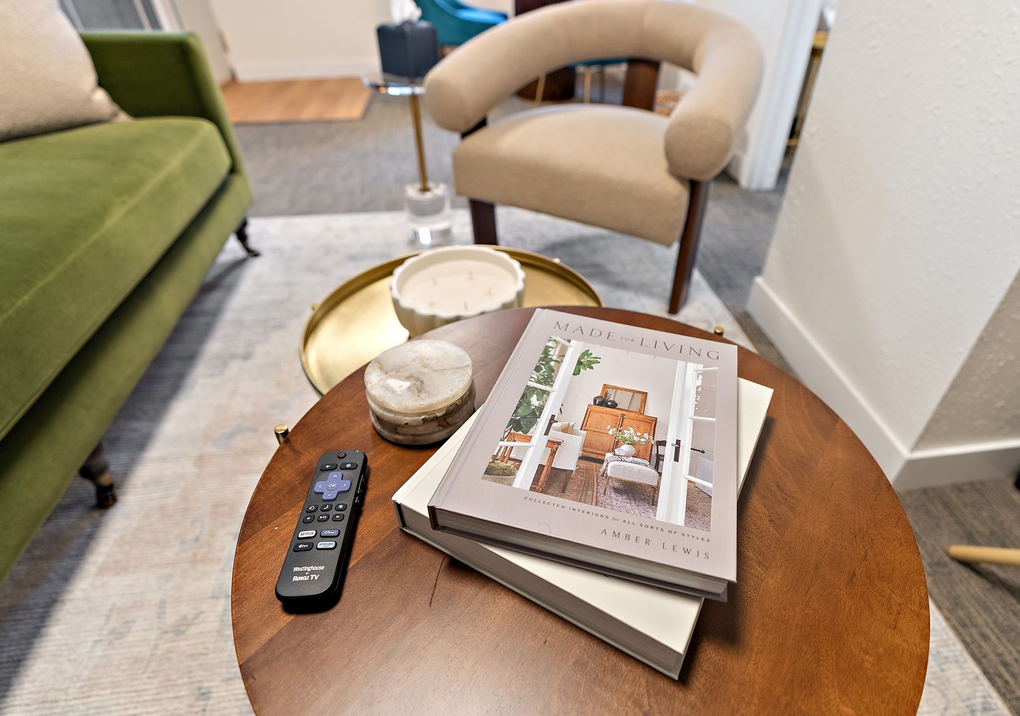 A remote control, a book titled 'Made for the Living', and a round wooden table in a living room.