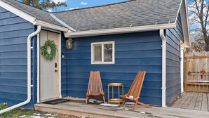 A blue house with a front door, a window, and two wooden chairs on the porch. - Charming 2-bedroom cottage in delightful Willmar with WiFi, AC (Willmar)
