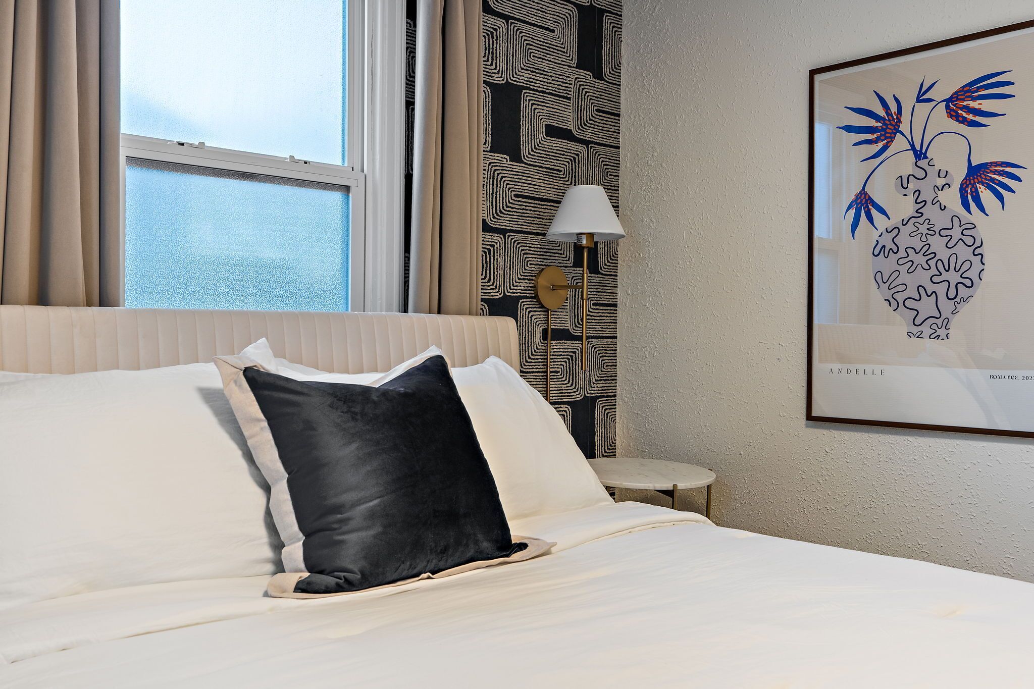A hotel room with a bed, a nightstand, a lamp, and a patterned wall.