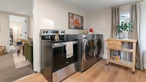 A compact kitchen with a built-in oven, a washing machine, and a wooden cart with storage. - Charming 2-bedroom cottage in delightful Willmar with WiFi, AC (Willmar)