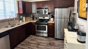 Una cocina con armarios de madera oscura, electrodomésticos de acero inoxidable, encimera de granito y suelo de madera.