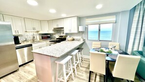 A modern kitchen with white cabinets, a granite countertop, and a dining area with a table and chairs.