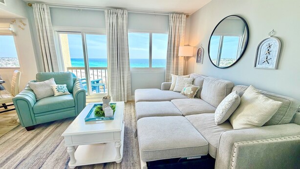 A living room with a view of the ocean, a blue armchair, a beige sofa, and a white coffee table.