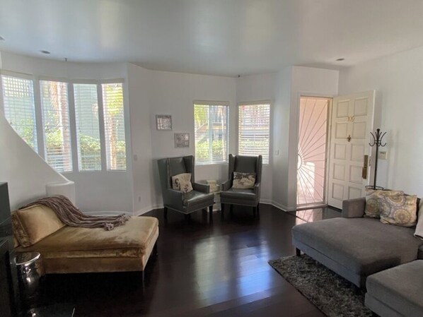 A spacious living room with a sofa, two armchairs, and a coffee table. Large windows allow natural light to fill the room.