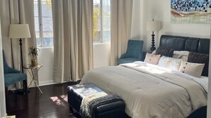 Un dormitorio con una cama grande, una mesita de noche, una lámpara y un ventanal con cortinas.