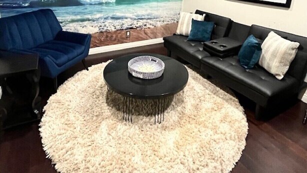 Una sala de estar con un mural de playa, un sofá de cuero negro, un sillón azul y una mesa de centro redonda.