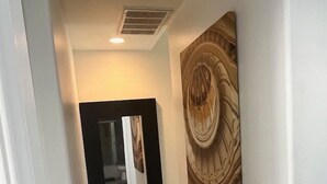 Un pasillo con un espejo de marco negro, un adorno de pared y una luz empotrada en el techo.