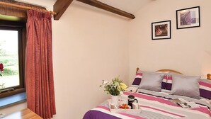 A bedroom with a bed, a wooden nightstand, a window with curtains, and two framed pictures on the wall.