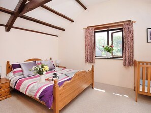 Un dormitorio con una cama de madera, una mesita de noche, un aparador, una ventana con cortinas y vistas al exterior con vegetación.