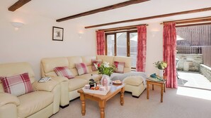 A cozy living room with a beige sofa, a wooden coffee table, and a window with red curtains. - Grandma's Cottage - UK48618 (Warbstow)