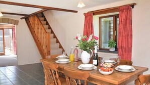 A dining area with a wooden table set for four, a staircase, and a window with red curtains.