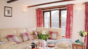 A cozy living room with a beige sofa, a wooden coffee table with snacks, and a window with red curtains. - Grandma's Cottage - UK48618 (Warbstow)