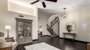 A spacious living room with a dark wood floor, a large cabinet, a staircase, and a round mirror on the wall. - Spanish Wells Scottsdale Oasis (Scottsdale)