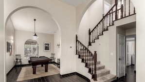 A spacious living room with a pool table, a staircase, and a view to the outdoors. - Spanish Wells Scottsdale Oasis (Scottsdale)