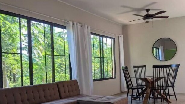 Un salon spacieux doté d’une grande fenêtre, d’un canapé, d’une table à manger avec des chaises et de deux ventilateurs de plafond.