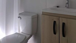 Une salle de bain avec des toilettes, un lavabo et un miroir. Il y a une étagère avec des articles de toilette et un tableau au-dessus du miroir.