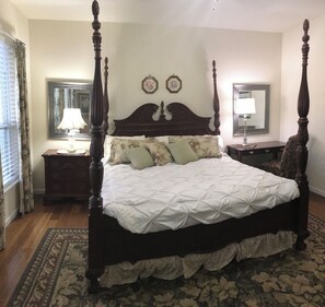 Ein Bett mit Baldachin, mit Blumenmuster bezogen, ein Nachttisch mit Lampe und ein Spiegel an der Wand.