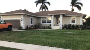A two-story house with a garage, a front lawn, and palm trees. - Charming remodeled waterfront home in marco island. (Marco Island)