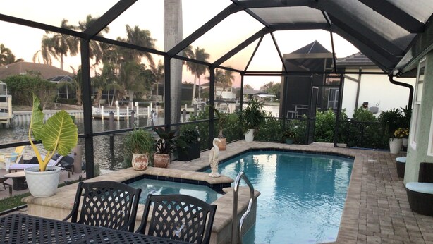 An outdoor pool area with a covered seating area, surrounded by potted plants and palm trees. - Charming remodeled waterfront home in marco island. (Marco Island)