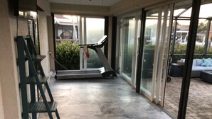 A covered outdoor area with a treadmill, a green metal chair, and a glass door leading to a patio with outdoor furniture. - Charming remodeled waterfront home in marco island. (Marco Island)