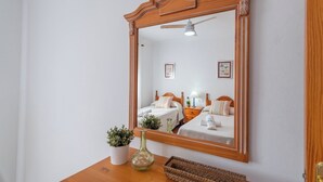A hotel room with a large mirror, two beds, a ceiling fan, and a small table with a plant and a vase.