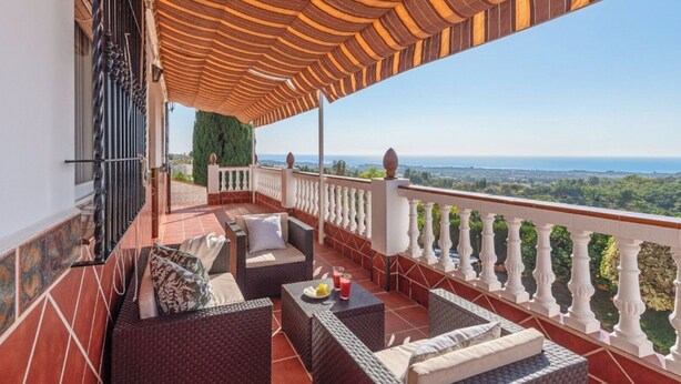 A balcony with wicker furniture, a table with a drink, and a view of the landscape.