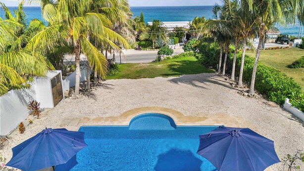 Una piscina con dos sombrillas, rodeada de palmeras y vista al océano.